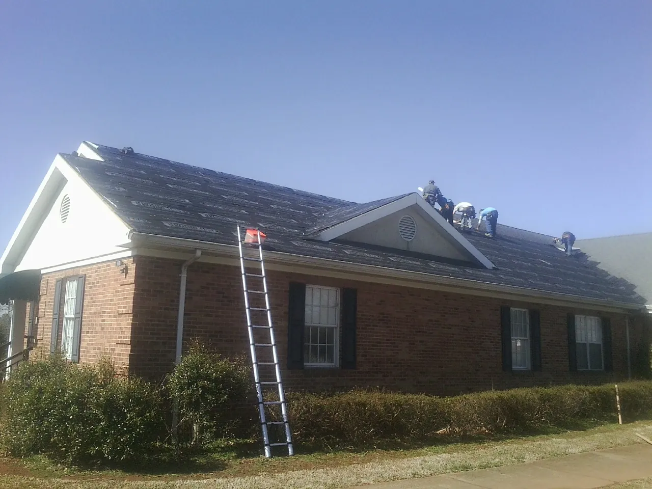 Crew tearing shingles off a brick ranch roof with a ladder set — Emergency Roof Repair work by our crew in Halfway