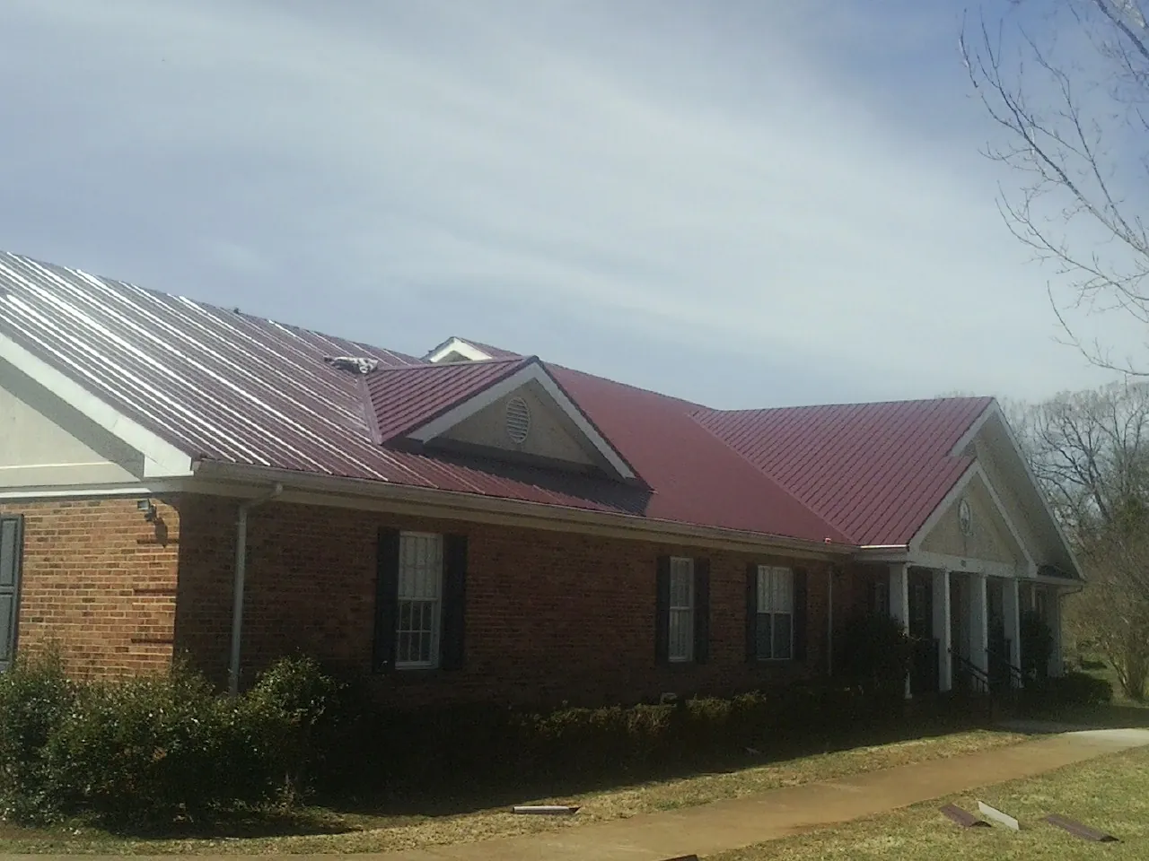 Red metal roof with gabled entries on a long brick building, from a Hail Damage Roof Repair job in Halfway
