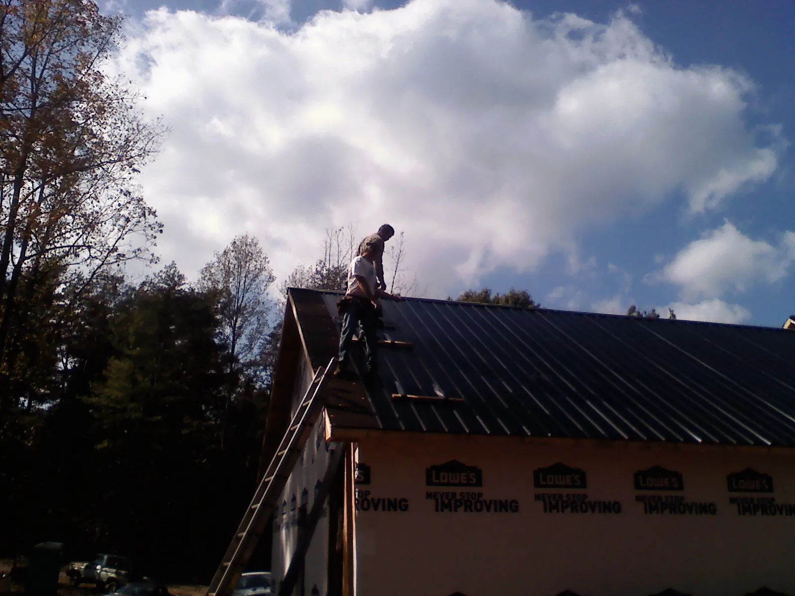Roofer fastening dark metal panels high against a cloudy sky, from a Roof Inspection job in Halfway