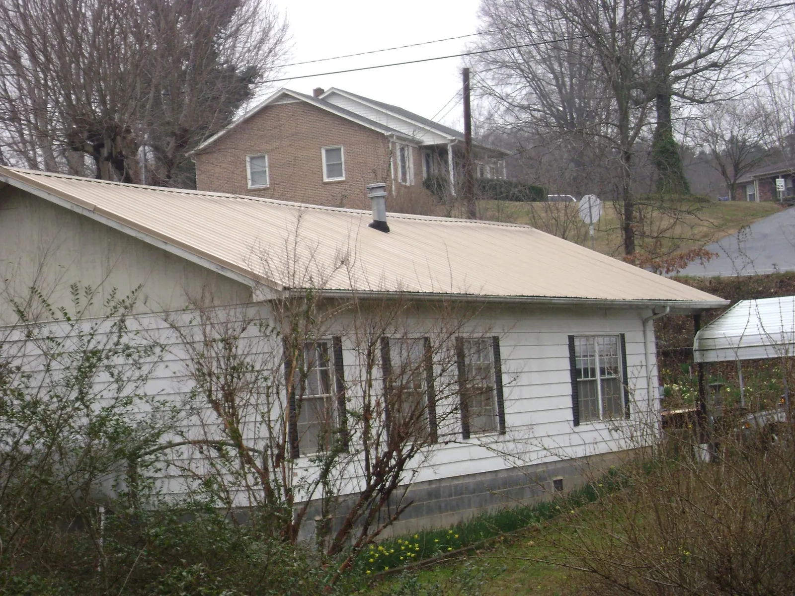 Tan metal roof on a white sided house set into a hillside — Commercial Roofing by Roofing Brothers in Halfway