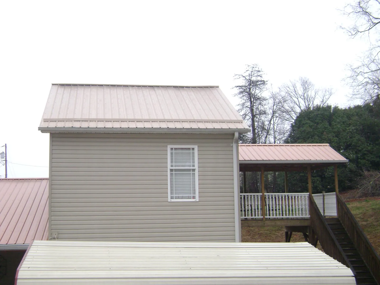 Tan metal roofs on a two story addition and attached porch, from a Roof Replacement job in Halfway
